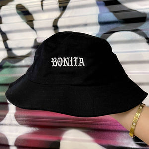 Viva La Bonita Women streetwear black Bonita Bucket hat. Hand holding black Bonita Bucket hat with graffiti background.